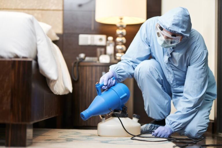 Technician in protective clothing applying electrostatic disinfectant