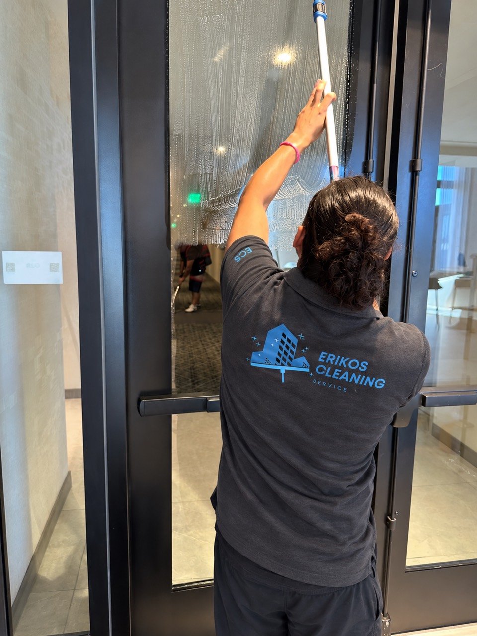 Eriko’s Cleaning team member washing a glass entrance door in a branded uniform
