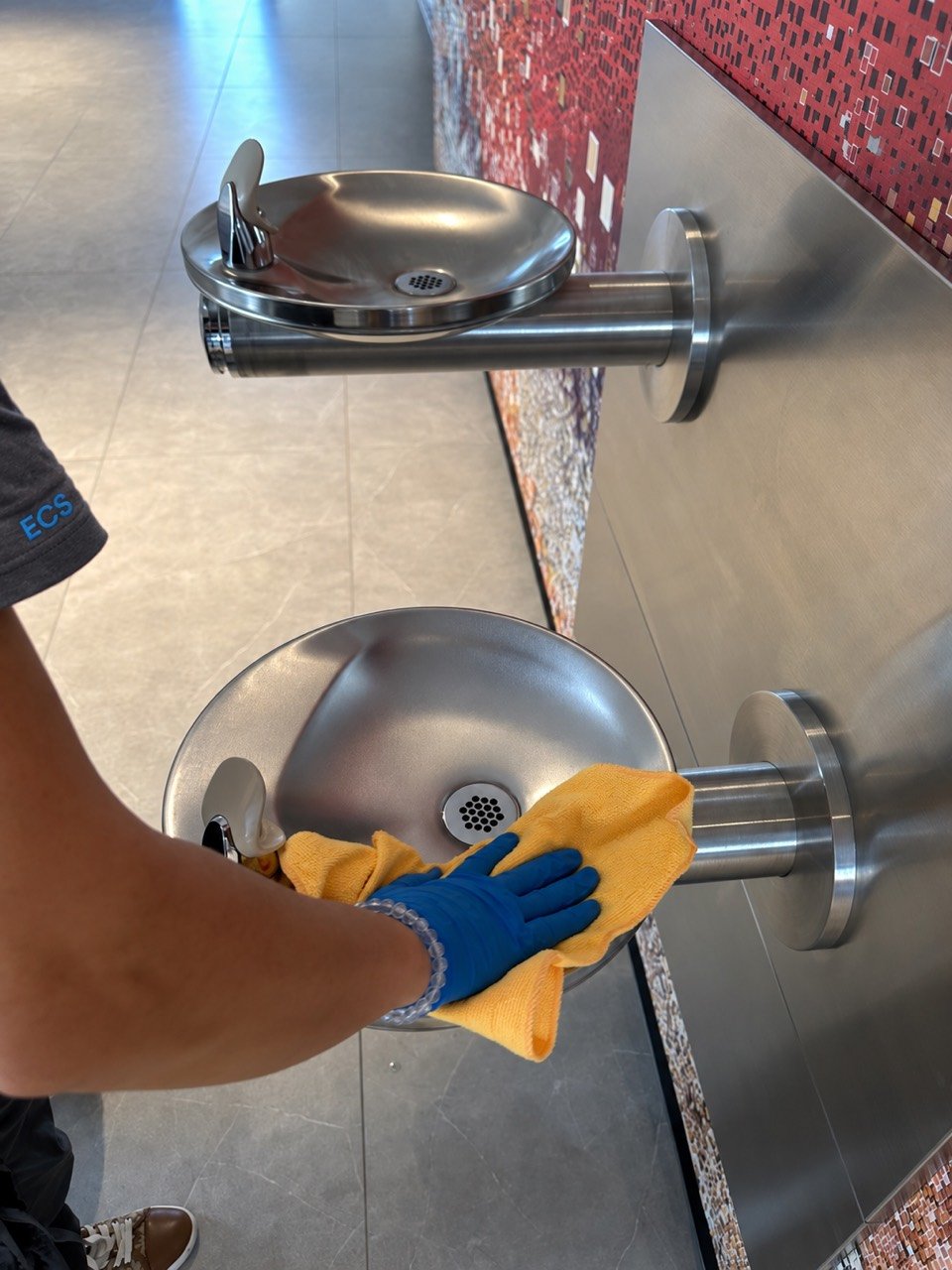 Gloved Eriko’s Cleaning team member wiping a stainless-steel drinking fountain