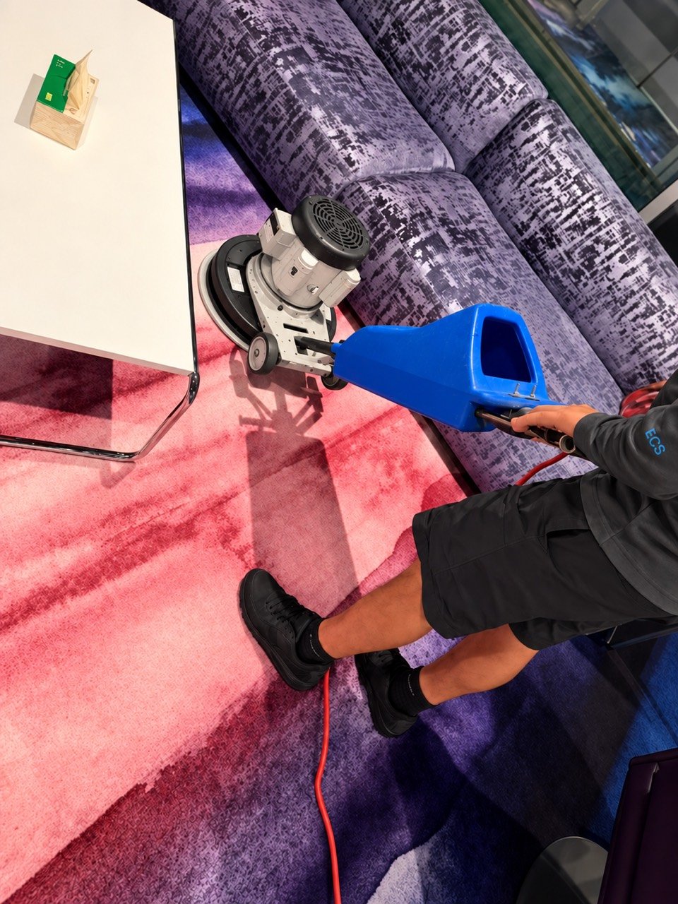 Eriko’s Cleaning team member using a rotary carpet-cleaning machine beside lounge seating