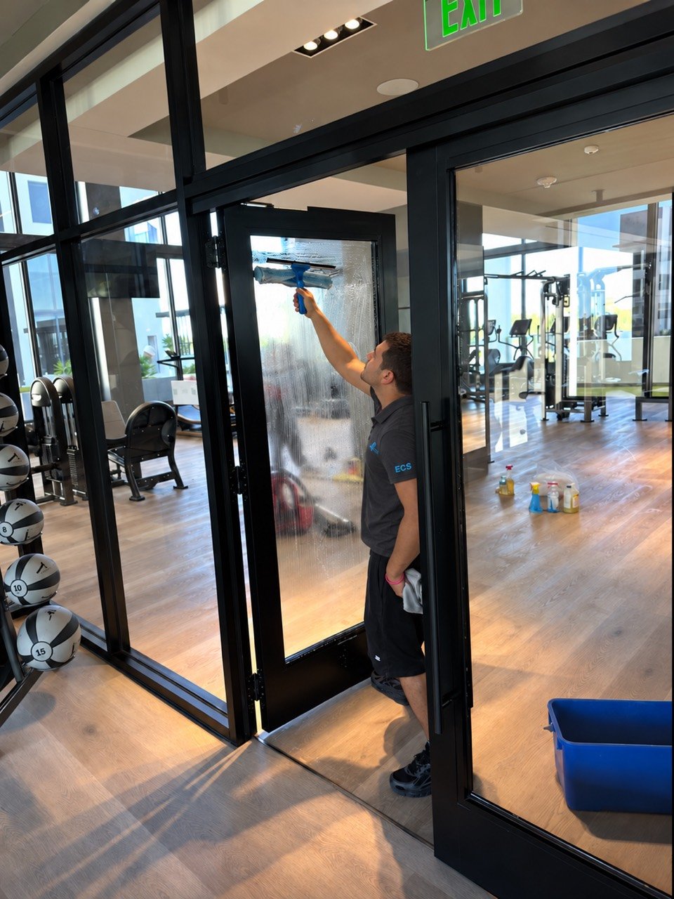 Eriko’s Cleaning team member washing a glass door beside a fitness area